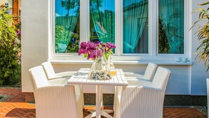 A white wicker outdoor seating area with a table, chairs, and a vase of flowers.