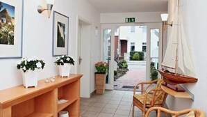 A reception area with a wooden console table, wicker chairs, potted plants, and a sailboat model.
