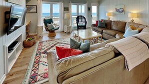 Een woonkamer met een televisie, twee banken, een salontafel en uitzicht op de oceaan.