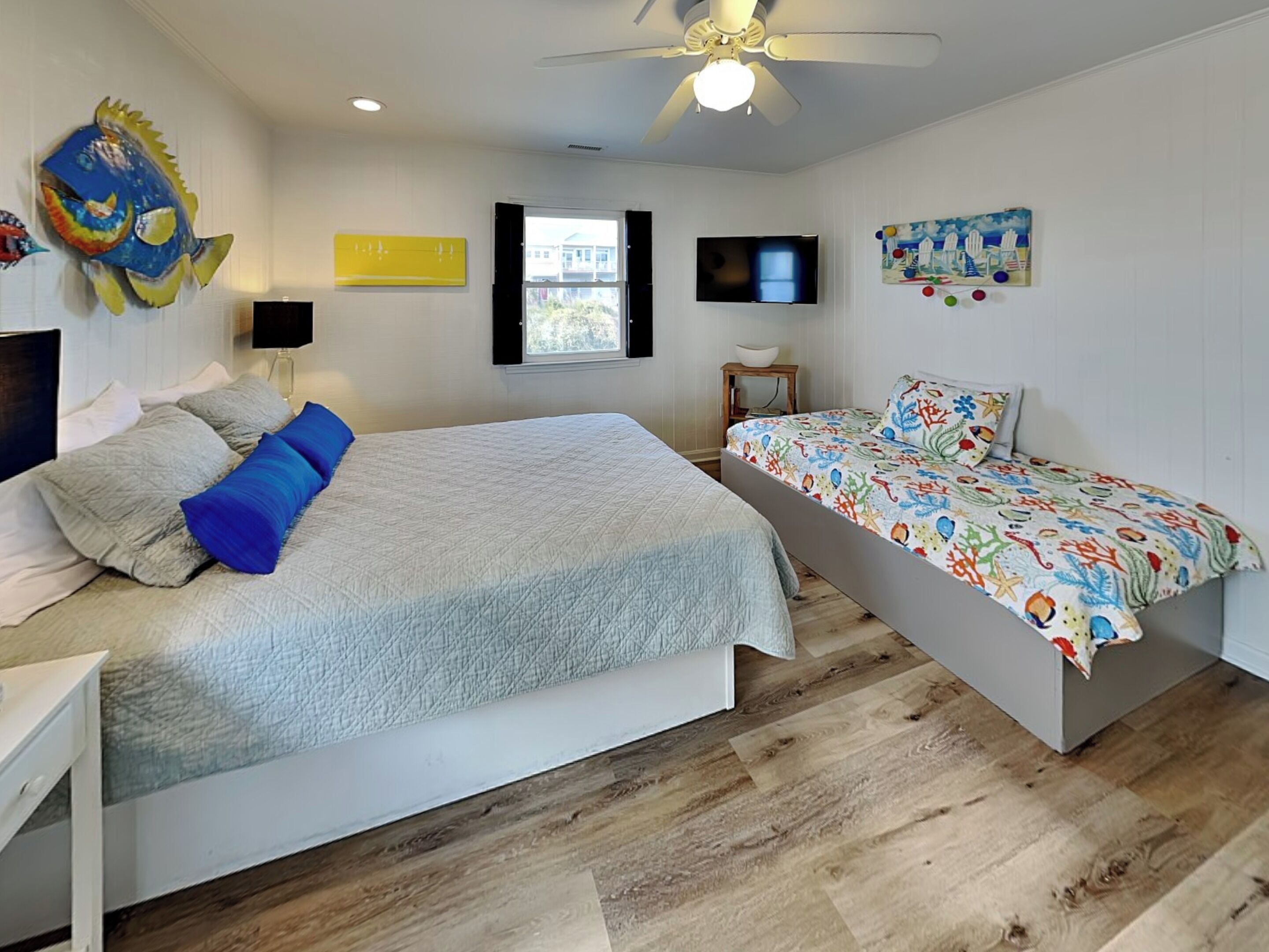 A bedroom with a large bed, a smaller bed, a ceiling fan, a TV, and a window.