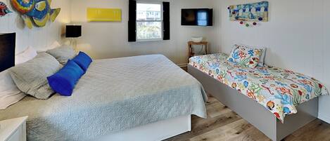 A bedroom with a large bed, a smaller bed, a ceiling fan, a TV, and a window.