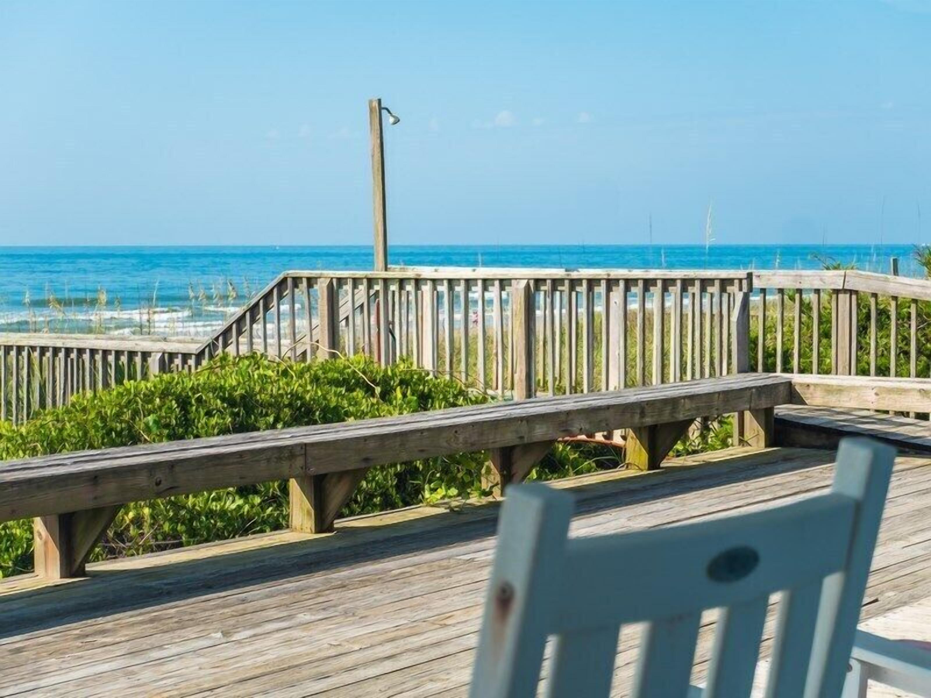 A wooden boardwalk leading to a beach with a bench and a lamp post.