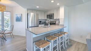 Une cuisine moderne avec des meubles blancs, des appareils en acier inoxydable et un coin bar avec des tabourets.