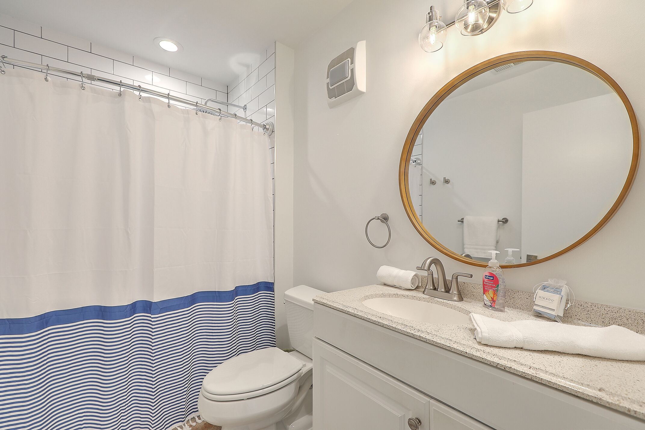 A bathroom with a shower curtain, toilet, sink with soap dispenser, and a mirror.