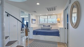 Une chambre à coucher avec un lit, une fenêtre avec des stores, un miroir et un escalier.