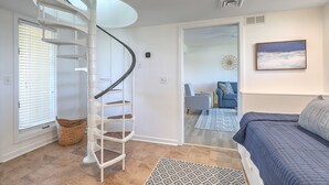 Une chambre avec un escalier en colimaçon, un lit, une chaise et une vue sur une autre pièce, visible à travers une porte vitrée.