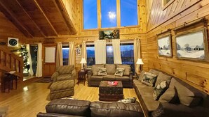 Ein gemütliches Blockhaus-Interieur mit einer großen Holzbalkendecke, einer Holz-Sofagarnitur und einem Kamin.