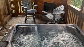 Un patio in legno con vasca idromassaggio, due poltrone Adirondack e un camino.