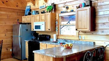 Interior de una cabaña de madera con cocina, que incluye un refrigerador, estufa, microondas y armarios de madera.