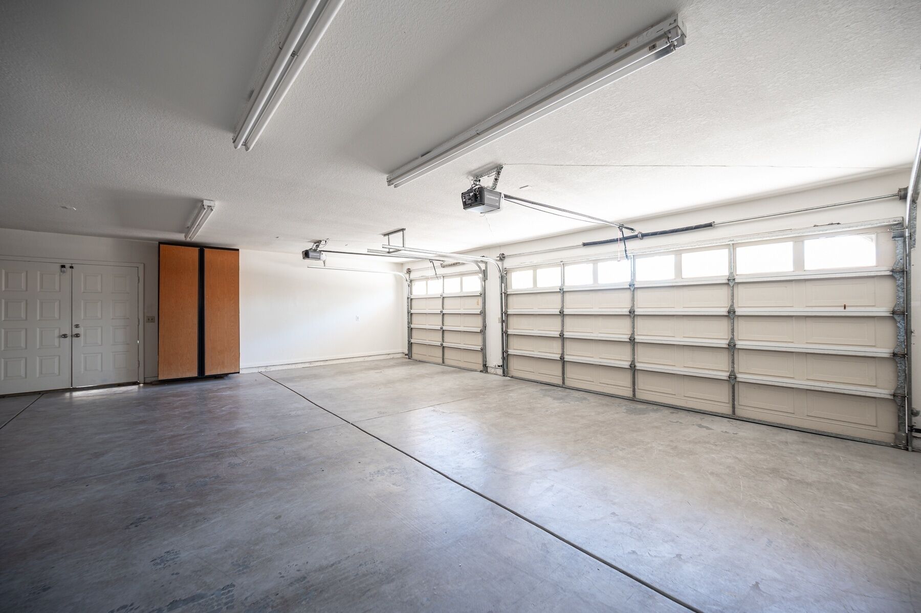 Un grand garage doté d ’un sol en béton, de portes de garage blanches et d’un éclairage fluorescent au plafond.