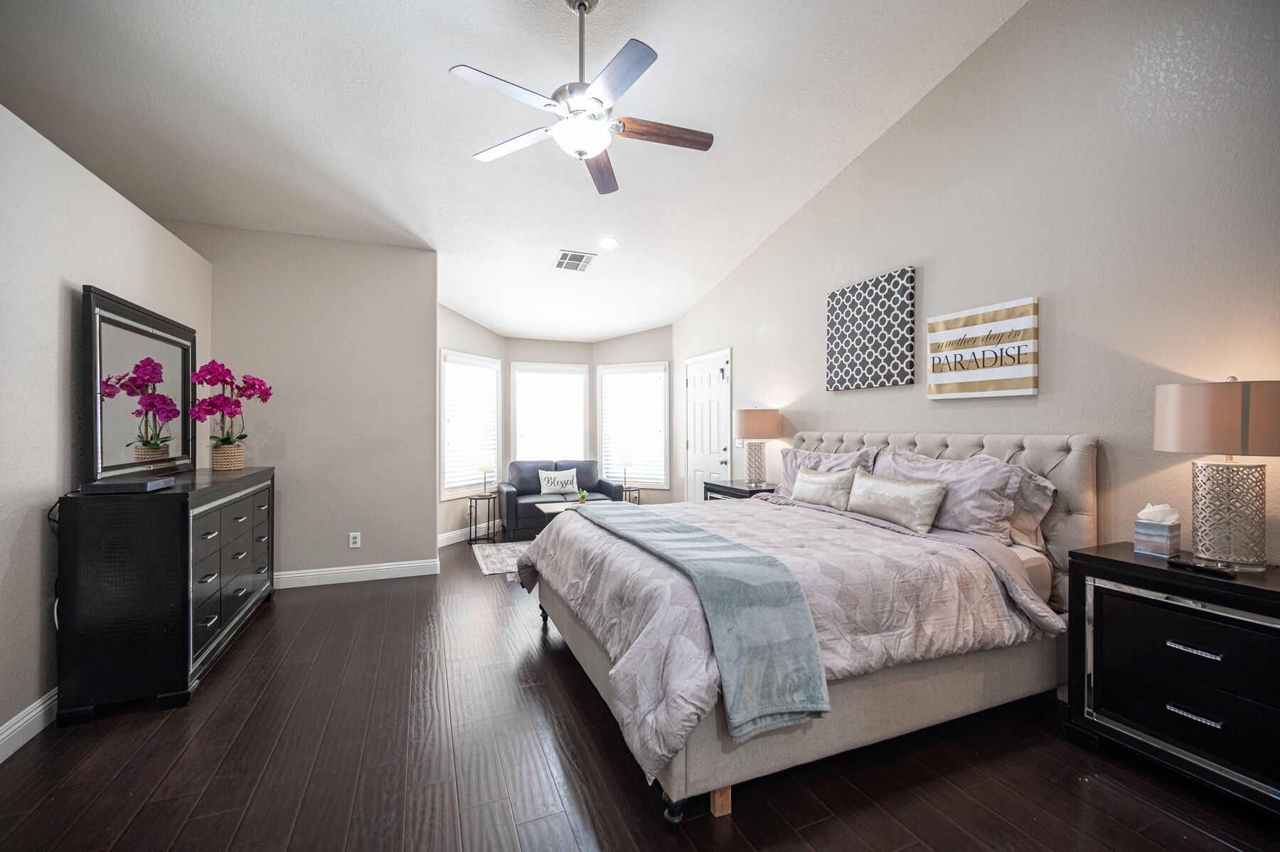 Une chambre à coucher comprenant un lit, une commode, une table de chevet et un ventilateur de plafond.
