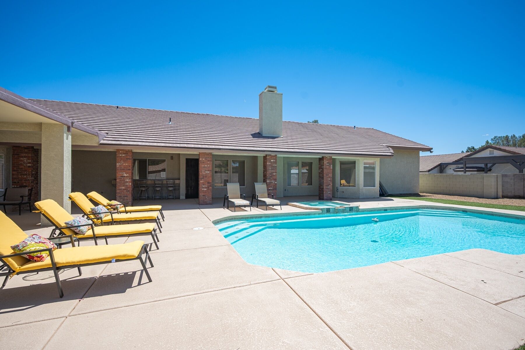 A residential property with a swimming pool, sun loungers, and a covered patio area.