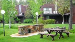 A stone fire pit with benches, surrounded by a well-maintained lawn and trees.