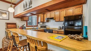 A kitchen with wooden cabinets, a black refrigerator, a microwave, and a dining area with wooden chairs and a bar.