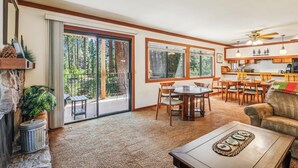 A spacious living area with a large sliding glass door leading to a balcony, a dining area with wooden furniture, and a kitchen with wooden cabinets and a ceiling fan.