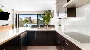 A modern kitchen with a large island, dark cabinets, and a view of buildings through the glass door.