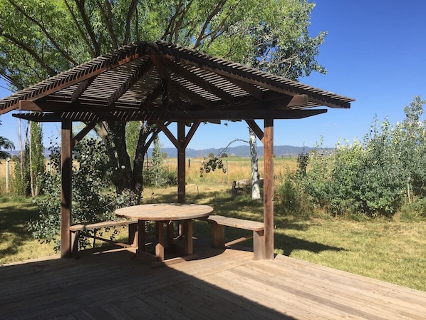A wooden gazebo with a bench and picnic table, surrounded by trees and grass. - Sun Mesa House (Durango)