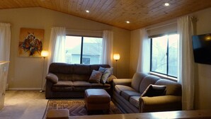 Uma sala de estar acolhedora com teto de madeira, dois sofás, uma mesa de centro e uma televisão de tela plana fixada na parede.