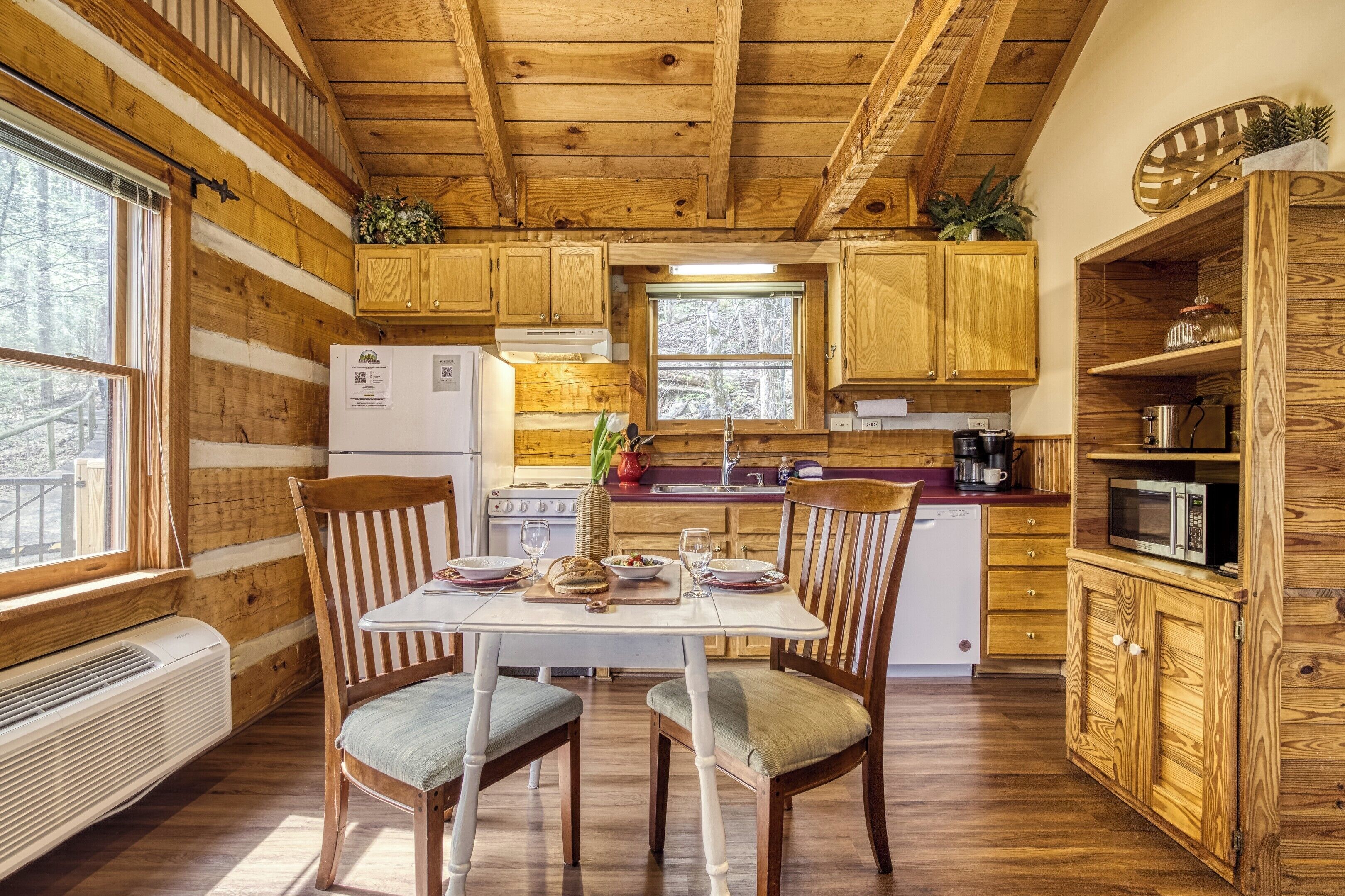 A cabin-style kitchen with wooden walls, a dining table with chairs, a refrigerator, a stove, and a microwave.