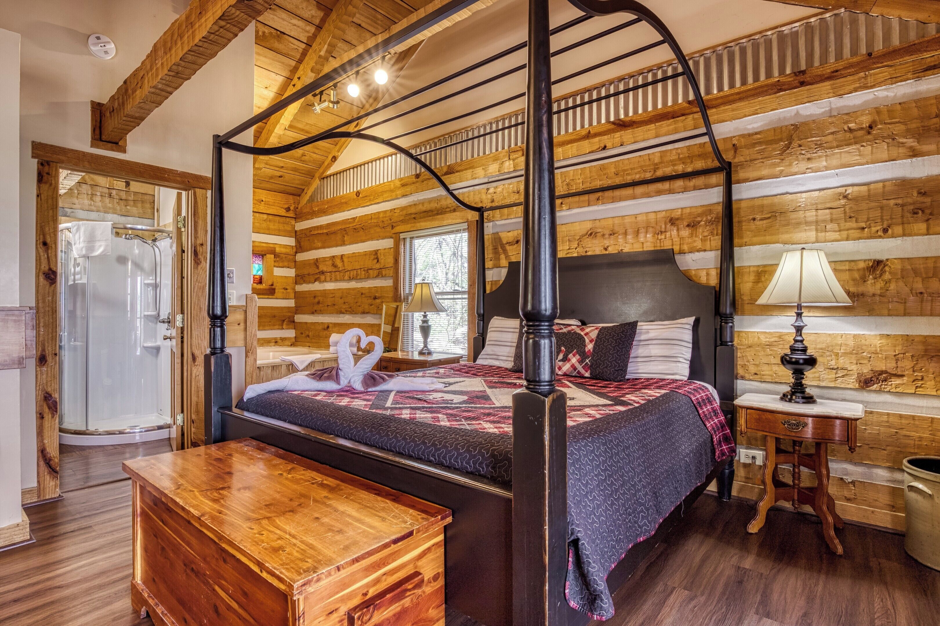 A four-poster bed with a wooden headboard, a bedside table, a lamp, and a window with a view of trees.