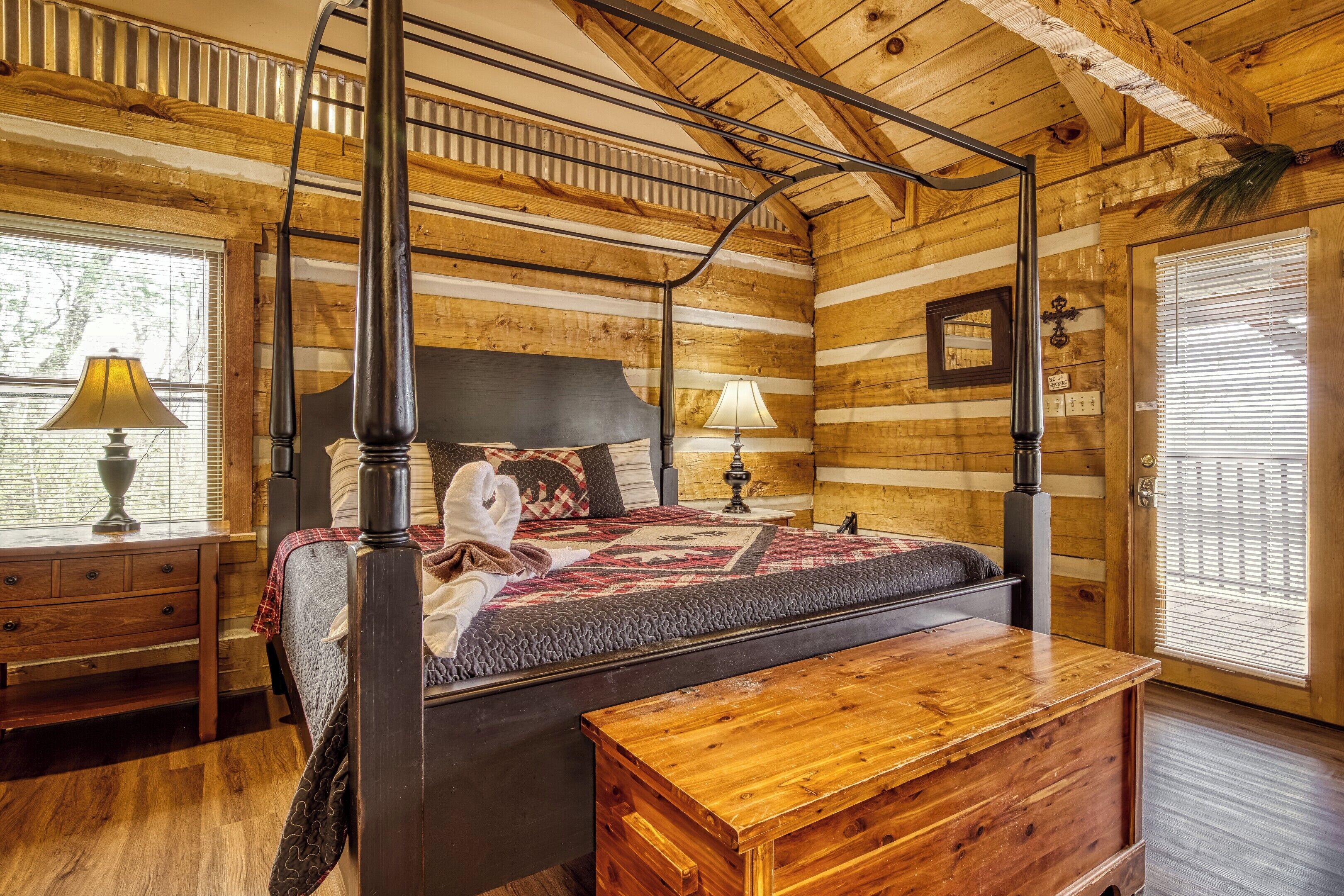 Un lit à baldaquin avec une tête de lit en bois, une table de chevet avec une lampe et un banc dans une pièce aménagée dans le style d’un chalet en rondins.