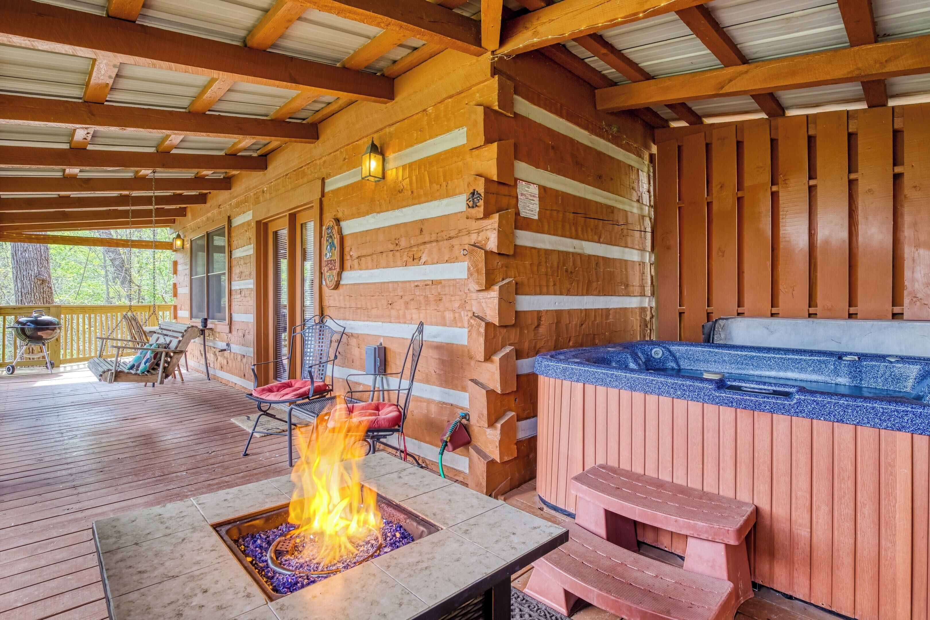 A covered outdoor area with a fire pit, seating, and a hot tub.