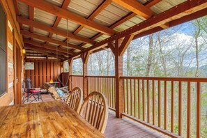 A wooden deck with a table and chairs, a fire pit, and a view of trees and mountains.