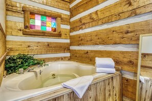 A wooden cabin-style bathroom with a bathtub, a wooden-framed stained glass window, and a mirror.