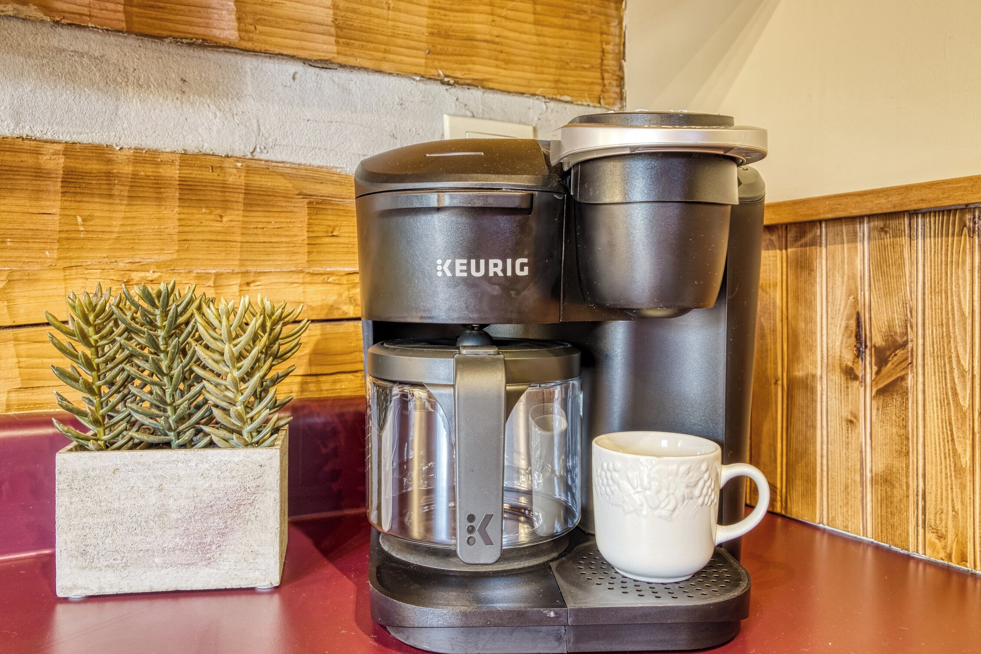 A Keurig coffee maker with a white mug and a potted plant on a wooden counter.