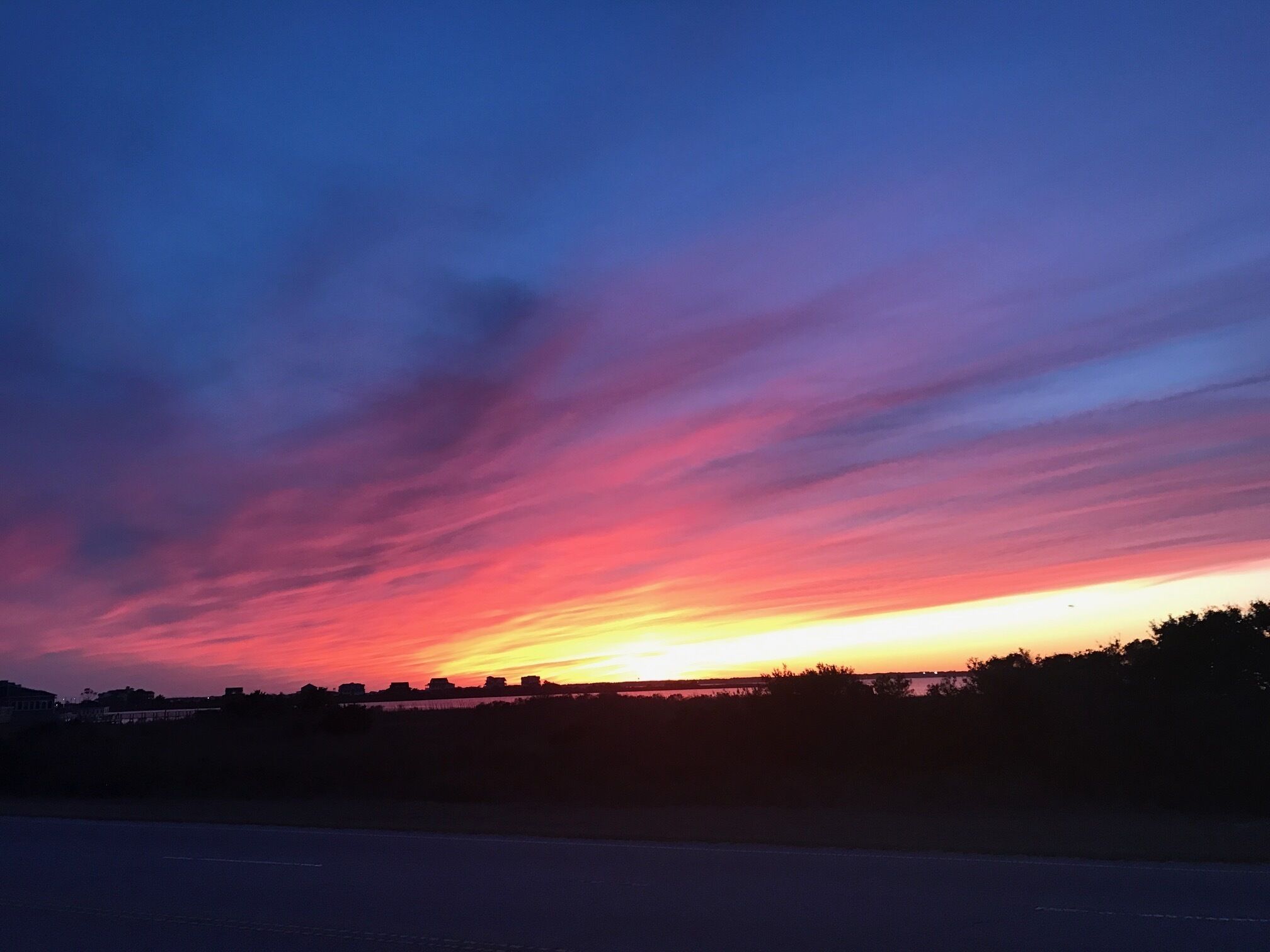 Un coucher de soleil sur une étendue d’eau, avec une route au premier plan.