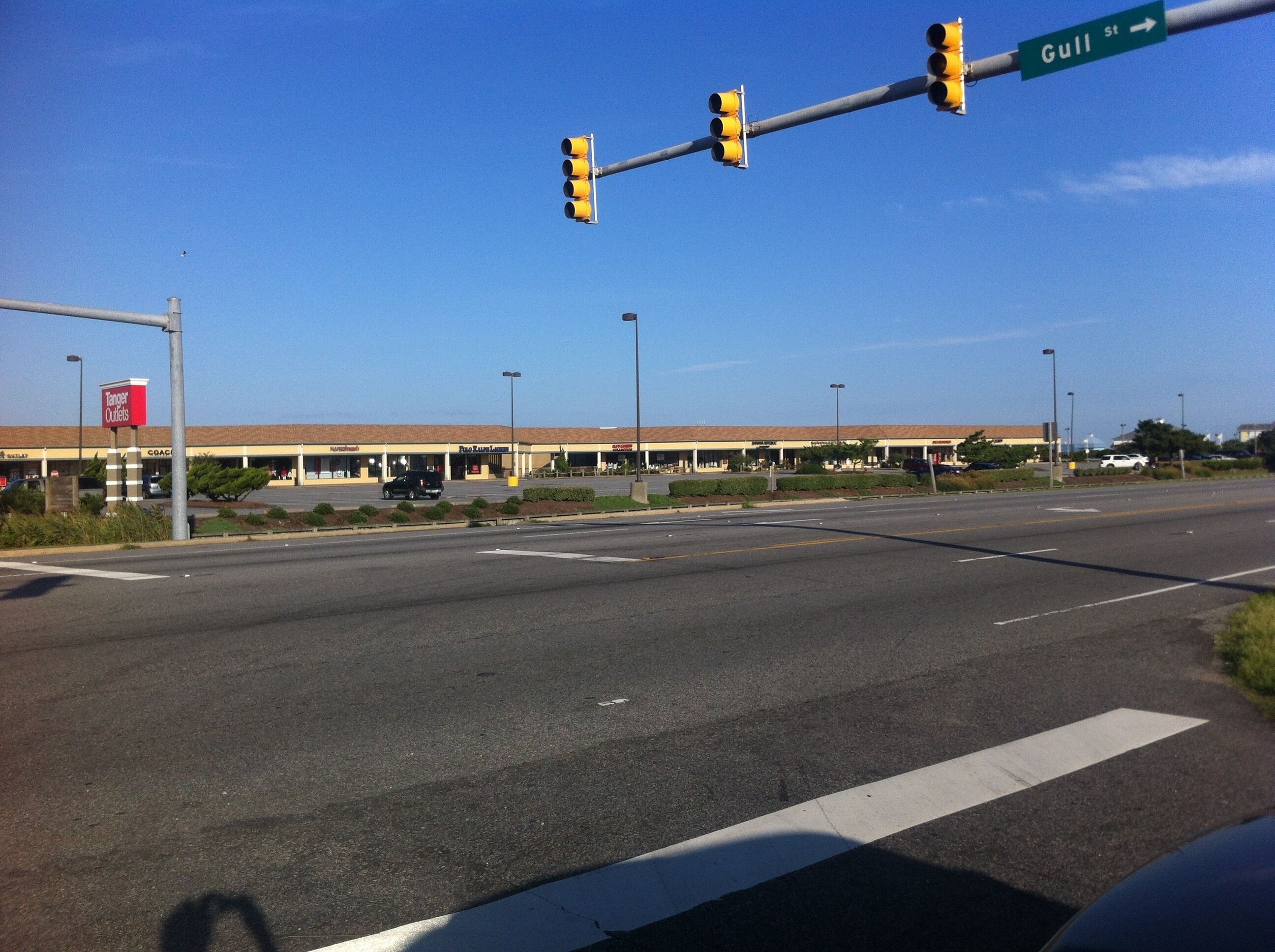 A street intersection with traffic lights and a store named 'Tanger Outlets' in the background.