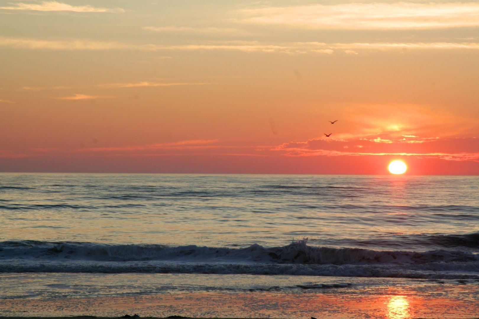 A sunset over the ocean with waves and birds in the sky.