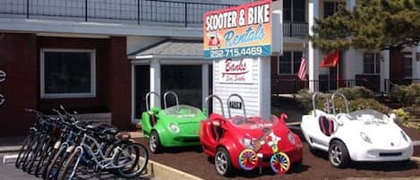 A building with a sign for scooter and bike rentals, a parking lot with bicycles, and a storefront with a sign for a bank.