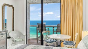 A room with a bed, a chair, a table, and a view of the ocean. - Free Beach SRVC! Direct Ocean Views! Free Beach Bonfires! Great Amenities! (Miramar Beach)