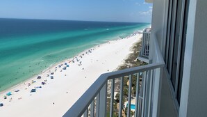 Blick auf einen Strand vom Balkon aus, mit blauem Himmel, Sandstrand und Poolbereich.