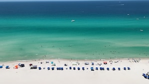 Ein Strand mit klarem türkisblauem Wasser, einem sandigen Ufer sowie mehreren Sonnenschirmen und Liegestühlen.