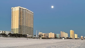 Ein Hotel direkt am Strand mit einer gewölbten Fassade, mehreren Balkonen und einem Sandstrand im Vordergrund.