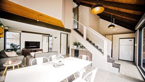 Eine moderne Küche mit weißen Schränken, ein Essbereich mit weißem Tisch und Stühlen sowie eine Treppe zu einer oberen Ebene.