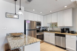 A modern kitchen with white cabinets, stainless steel appliances, granite countertops, and a hanging light fixture.