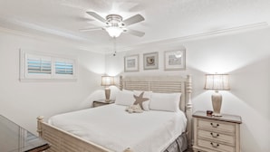Une chambre à coucher comprenant un lit, des tables de chevet, un ventilateur de plafond et des œuvres d’art murales.