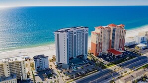 A coastal hotel with multiple high-rise buildings, a parking area, and a beach in the background.