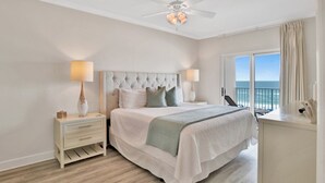 A bedroom with a bed, bedside tables, a ceiling fan, and a window with a view of the ocean.