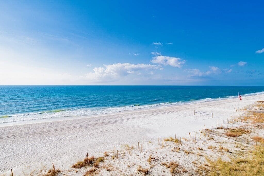 A beach with a clear sky, sandy shore, and a fence line.