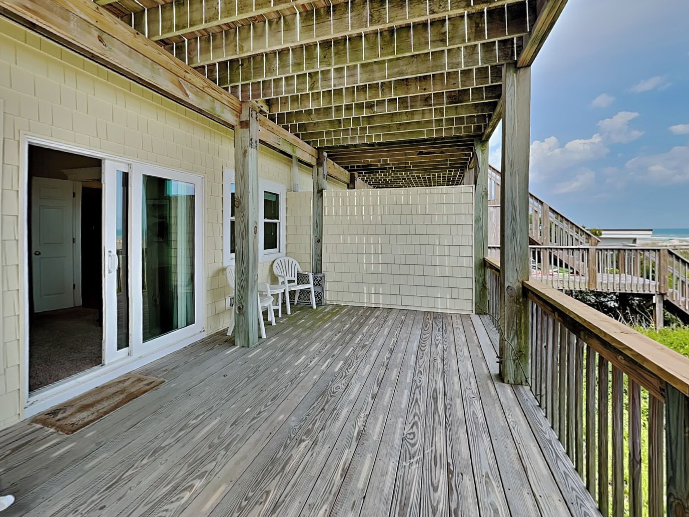 A wooden deck with a covered area, a sliding glass door, and a chair.