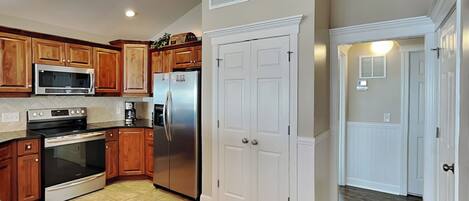 Cocina con armarios de madera, electrodomésticos de acero inoxidable y dos puertas blancas.