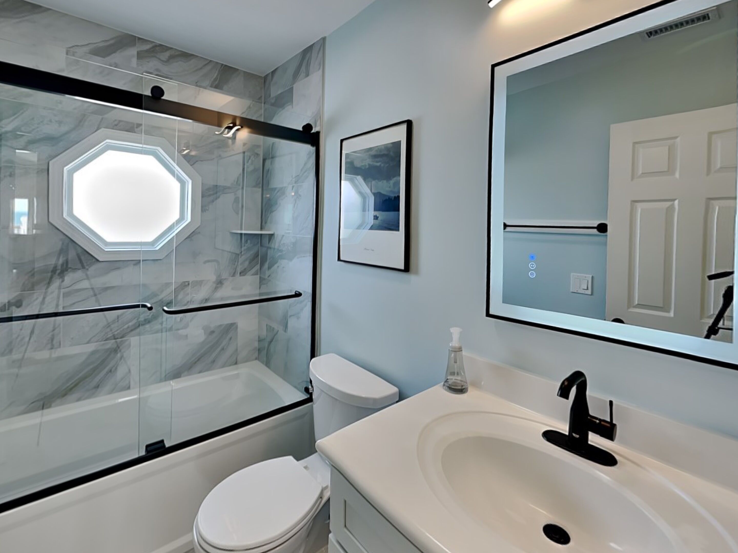 A modern bathroom with a glass shower enclosure, a white toilet, a sink with a black faucet, and a framed picture on the wall.
