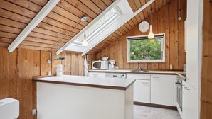 Kompakti keittiö, jossa on keskeinen saareke, puuseinät, kattovalokuvio ja ikkuna, josta avautuu näkymä vehreään maisemaan.
