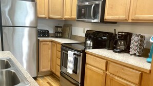 A compact kitchen with stainless steel appliances, wooden cabinets, and a granite countertop.