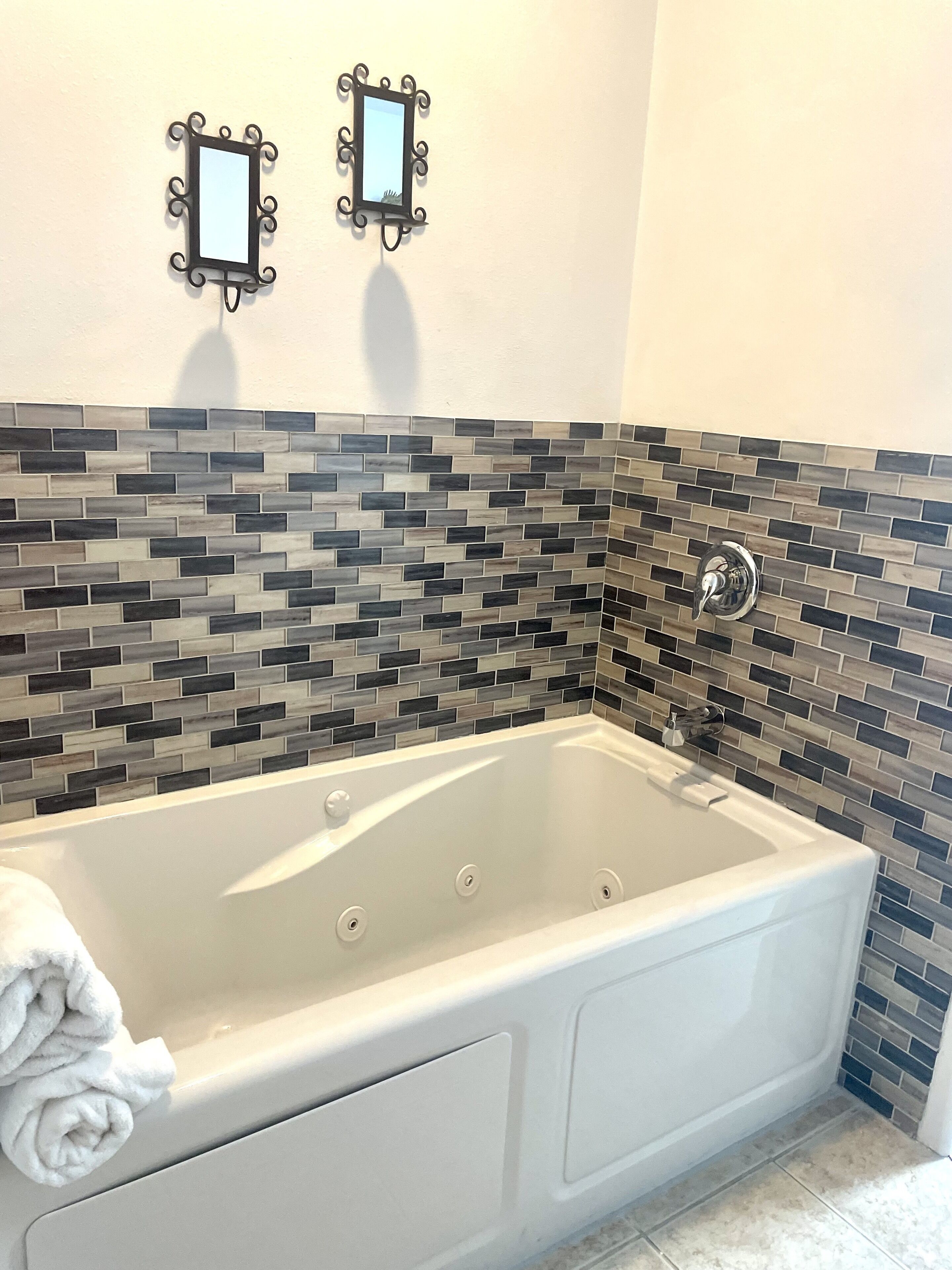 A modern bathroom with a freestanding bathtub, a tiled backsplash, and two wall-mounted mirrors.
