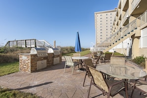 An outdoor patio with a grill, seating, and a view of a building.